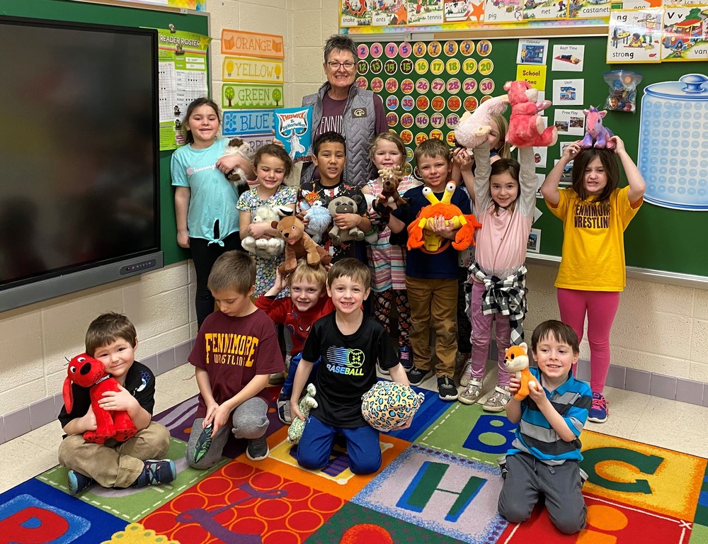 Mrs. Burkum stands with young students holding their stuffed animals after she reads a book to them.