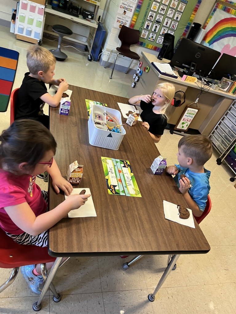 students sit at a table and munch on their cookies and drink their milk