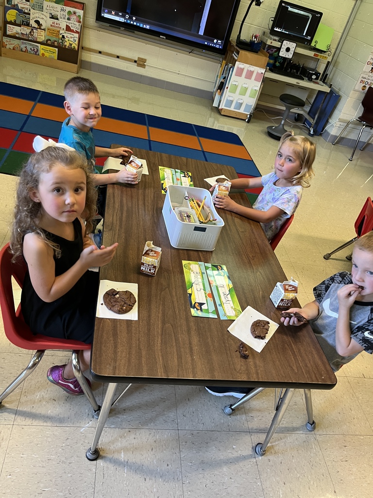 students sit at a table and munch on their cookies and drink their milk