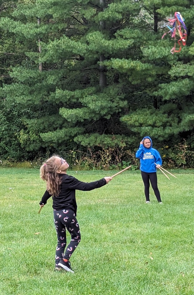 students play a colonial game outside with a stick and a colorful object