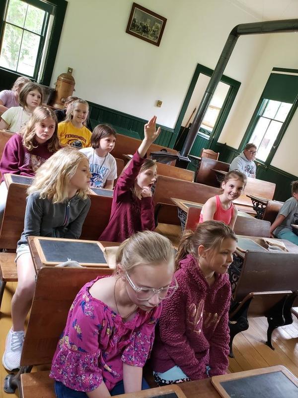 Students sit inside and old school house in desks
