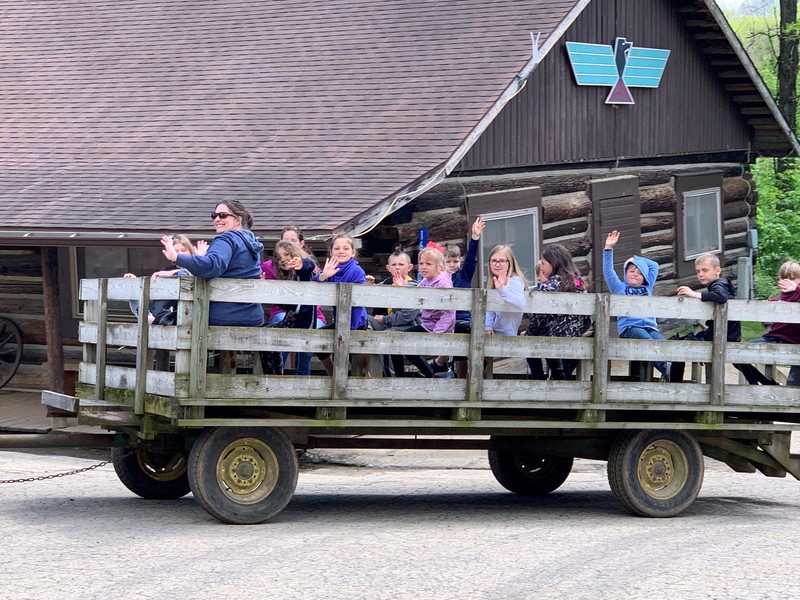 young students and their teacher ride in a wagon and wave