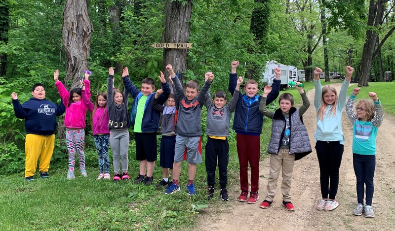 Students near a trail stand in a line with arms in the air